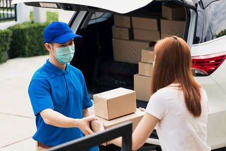 亚洲青年送货员在线采购亚洲青年送货员给他包裹邮箱保护面罩和女服务客户在前家门接受箱套根据宵禁大流行的科罗纳COVID19图片