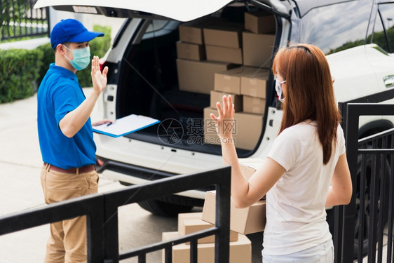 在女顾客收到箱子后亚洲年轻送货员手举道别女顾客收到箱子后两个保护面罩都戴着防在前门的宵禁检疫大流行冠状COVID19图片