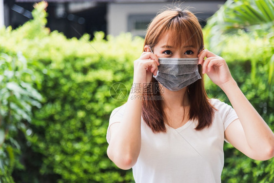 身戴面罩的亚洲青年妇女在绿色自然背景的检疫大流行冠状COVID19下在户外佩戴保护面罩图片