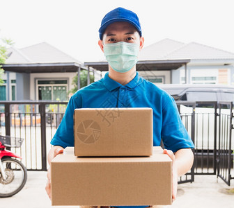亚洲快递年轻男子利用给女客户的箱子他在家门口根据宵禁检疫大流行冠状COVID19戴保护面罩图片