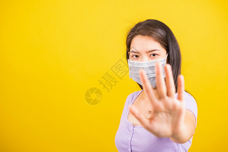 身戴面罩的亚洲少女妇戴面罩防止冠状或COVID19或过滤灰尘空气污染将手举到没有或停止的标志处孤立黄色背景图片