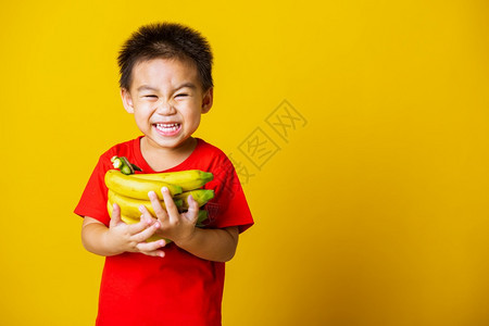 带着红色T恤的笑脸拿着香蕉梳子果拍摄室以黄色背景隔离图片