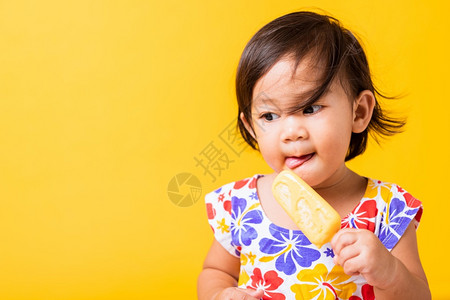 快乐的亚洲小婴儿或孩可爱的女快乐肖像笑有吸引力的小女孩笑穿着鸡样衬衫并吃甜木冰淇淋摄影棚拍着黄色背景夏季概念图片