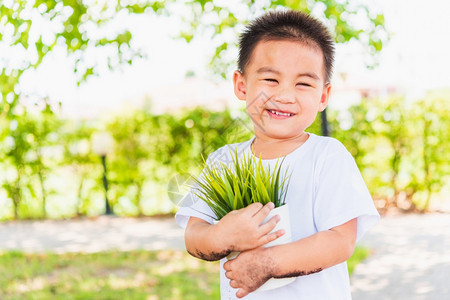 世界环境日与拯救世界概念亚洲可爱的快乐小男孩手在绿色花园背景下在白锅上抓着小树图片