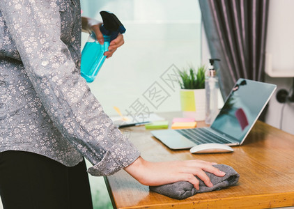 亚洲商业女青年在家庭办公室工作他清洁笔记本电脑用清洁剂酒精喷洒隔离疾病冠状毒或COVID19在工作前佩戴保护面具图片