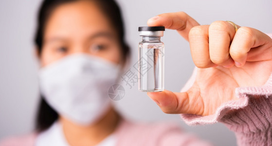 身穿外科保护布面罩的亚洲女医生面戴罩防止冠状她持有的氨水瓶疫苗侧重于玻璃透明工作室拍摄孤立的白色背景COVID19概念图片