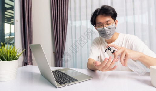 亚洲商人年轻英俊帅男眼镜在家办公室工作他隔离疾病冠状毒或COVID19戴防护面具在前笔记本电脑上用防污胶洗手图片