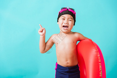 暑假概念肖莱特亚洲快乐可爱的小男孩穿着护目镜和泳衣抓着西瓜的充气环基德在暑假玩得开心工作室拍摄孤立的蓝背景图片