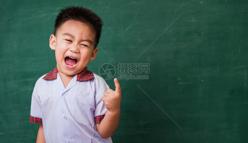 快乐的亚洲可爱小孩男从幼稚园学生制服微笑指在绿色学校的黑板上空间相邻第一次到学校教育概念图片