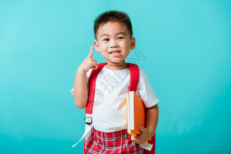 长相快乐的可爱亚洲小孩男笑着拥抱书和指向空间孤立的蓝背景图片