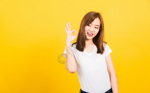 亚洲快乐肖像美丽可爱的年轻女孩站着穿T恤衫展示用手指好标志寻找孤立的侧面黄色背景摄影棚拍复制文本空间图片