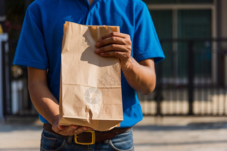 亚洲青年送货员网络上亚洲青年送货员配有食品订单取走纸袋集装箱他保护面罩根据宵禁检疫大流行冠状COVID19在前屋服务客户图片