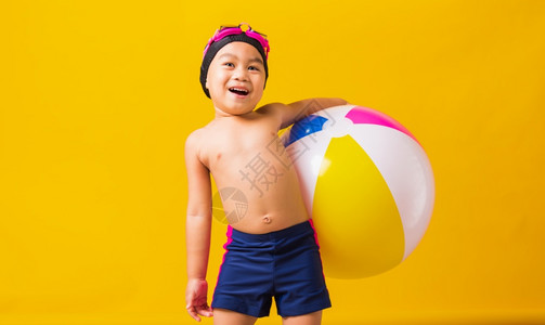 暑假概念肖写亚洲快乐可爱的小孩男笑在泳衣上沙滩球小孩在暑假和充气球玩得开心工作室拍摄孤立的黄色背景图片