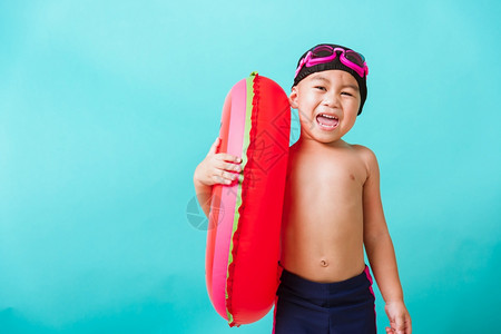 暑假概念肖莱特亚洲快乐可爱的小男孩穿着护目镜和泳衣抓着西瓜的充气环基德在暑假玩得开心工作室拍摄孤立的蓝背景图片