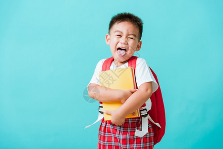 长相快乐的可爱亚洲小男孩笑拥抱书摄影棚拍孤立的蓝背景图片