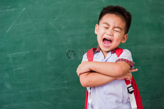 快乐的亚洲可爱小孩男从幼儿园穿着学生制服和校的背包站着微笑交叉手臂在绿色学校的黑板上第一次到学校教育概念图片