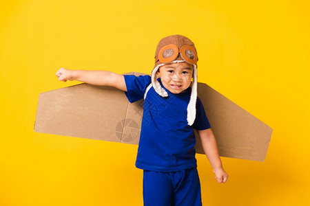 快乐的亚洲帅滑的小孩或男笑时戴着飞行员帽子玩耍和护目镜具纸板机翼飞行工作室拍摄孤立的黄色背景启动自由概念图片