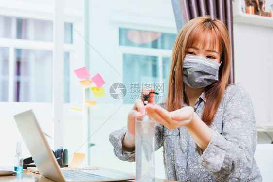 身戴面罩的亚洲年轻商业妇女身戴面罩在家庭办公室用笔记本电脑工作用笔记本电脑隔离冠状或COVID19疾病用清洁剂酒精凝胶泵洗手图片