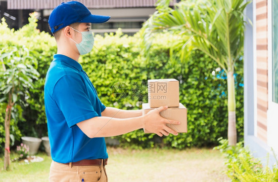 亚洲快递年轻男子利用给女客户的箱子他在家门口根据宵禁检疫大流行冠状COVID19戴保护面罩图片