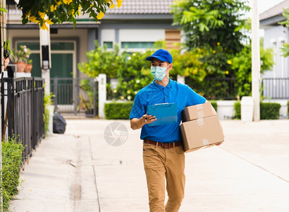 亚洲青年送货员信使携带包裹邮箱保护面罩服务在宵禁大流行的COVID19下步行寻找客户住家地点图片