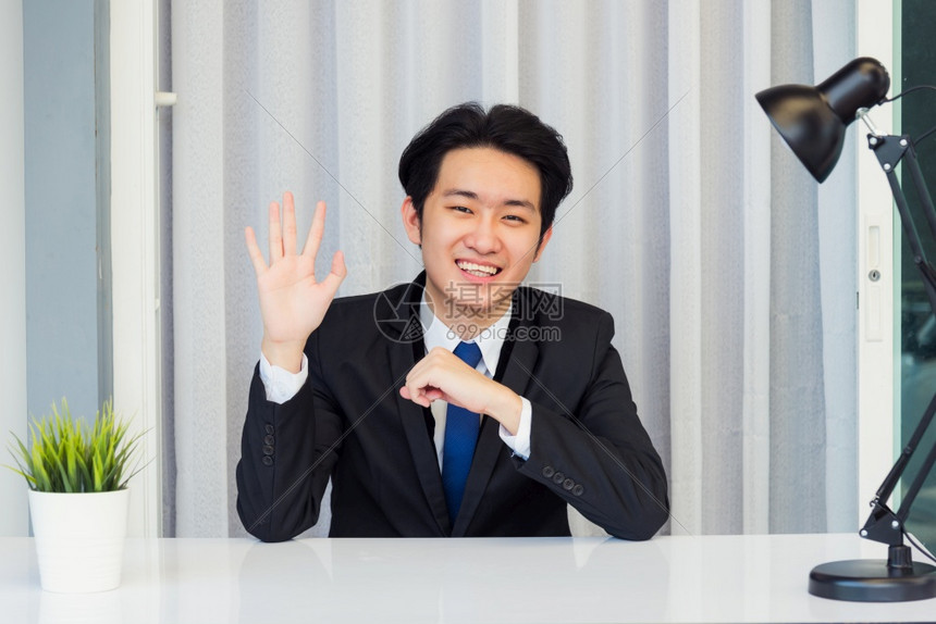 在家工作近面对亚洲青年商人的视频会议电话或面对时他看着照相机坐举起你的手在办公室桌上打招呼小组或客户图片
