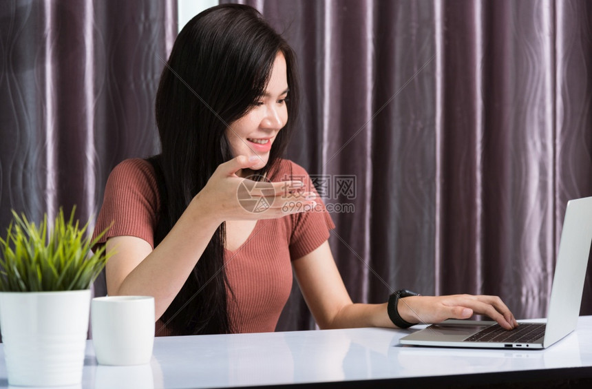 在家工作笑的亚洲快乐商业年轻美丽的女坐在办公桌间视频电话会议上使用网络摄像机手提电脑技术举起手来解释家庭办公室的工作图片