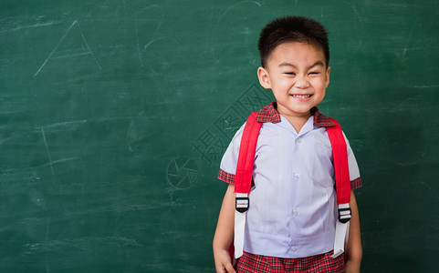 可爱小男孩穿着校服站在绿色校黑板上微笑图片