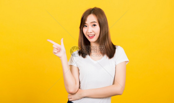 亚洲快乐肖像美丽的可爱年轻女孩站着穿T恤衫指向另一边看着镜头被孤立图片