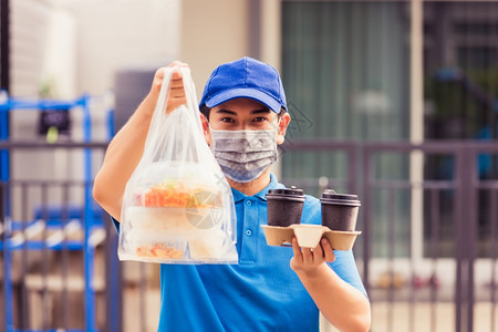 身着蓝制服的亚洲青年送货员戴面罩提供杂货服务根据流行冠状在前屋提供大米食品盒塑料袋和咖啡回到新的正常概念图片