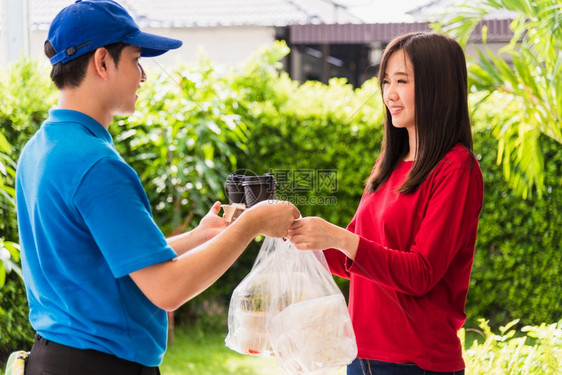 身穿蓝制服的亚洲年轻接生男青年他做杂货服务向根据流行冠状接受前门服务的妇女客户提供大米食品箱塑料袋回到新的正常概念图片