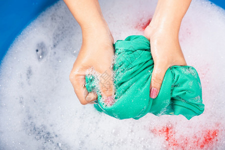 紧闭的亚洲年轻女在盆地用手洗彩衣物女用洗涤剂挤的湿布有水中肥皂泡工作室拍摄背景洗衣概念图片