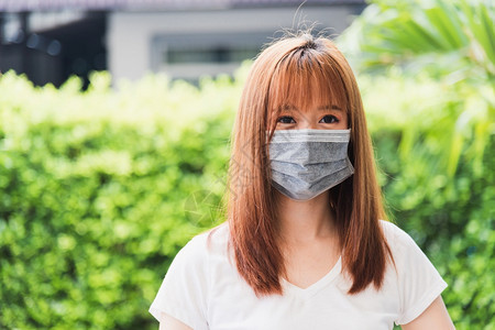 身戴面罩的亚洲青年妇女在绿色自然背景的检疫大流行冠状COVID19下在户外佩戴保护面罩图片