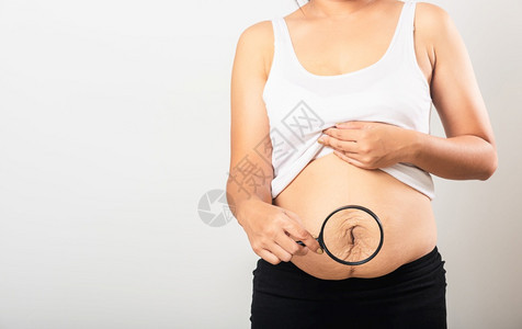 亚洲母女特写镜头用放大镜显示妊娠纹松弛的小腹皮肤她怀孕后肥胖婴儿出生隔离在白色背景上健康的腹部多余的身体概念图片