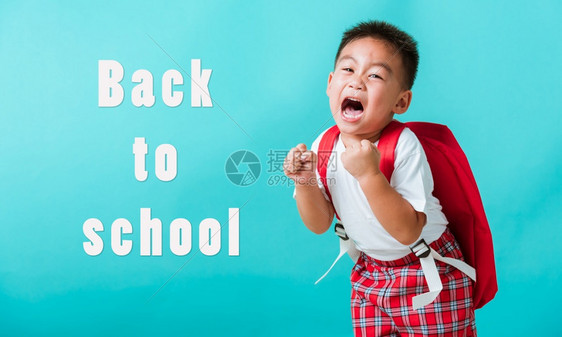 穿着制服笑脸的亚洲可爱男孩回到学校时举起手来欢庆孤立的蓝背景幼稚园时带着背包的孩子图片
