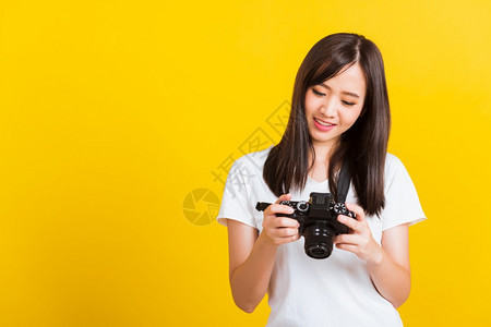 亚洲美丽年轻女摄影记者回顾照片时看到在数码无镜摄影机屏幕上拍照片在黄色背景上被孤立图片