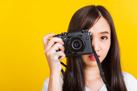 快乐的亚洲美丽年轻女摄影师的肖像正在拍照取景器上的复古数码无镜相机准备拍摄摄影棚拍摄的黄色背景上孤立图片