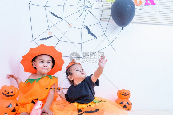 快乐的可爱小兄弟男孩和小女穿着万圣节服装和橙南瓜杰克与Cobweb和黑气球在家中白色墙背景快乐万圣节概念图片