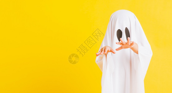 有趣的万圣儿童概念关闭一个可爱的小孩穿着白色服装的神圣的鬼魂吓坏了摄影棚拍孤立的黄色背景背景图片
