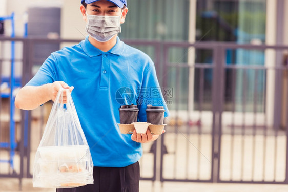 身着蓝制服的亚洲青年送货员戴面罩提供杂货服务根据流行冠状在前屋提供大米食品盒塑料袋和咖啡回到新的正常概念图片