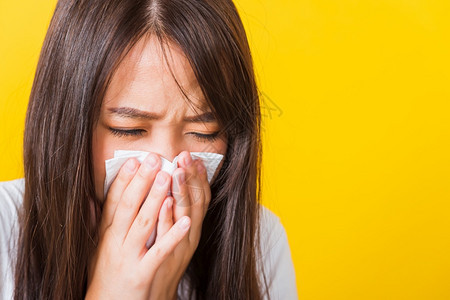 哭着用组织擦掉肌肉紧贴着正在打喷嚏的漂亮女孩使用毛巾擦鼻涕摄影棚拍在黄色背景上被孤立图片