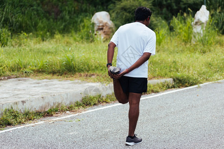 特写亚洲年轻运动员运动跑步者黑人男子戴手表抬脚伸展腿部和膝盖在户外街道健康公园跑步前锻炼前的健康锻炼概念图片