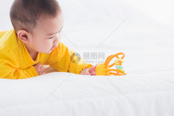 美丽的年轻亚洲新生儿小宝在家中的床上笑快乐的婴儿微穿着黄色衬衫在房间里放松图片