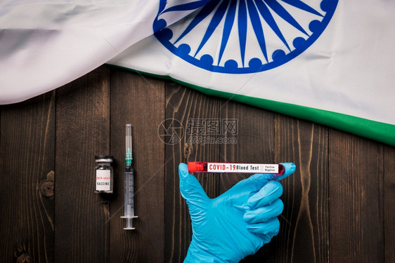 一名在实验室内戴手套持有验血管冠状COVID19COVID19的医生手挂印度旗着木制背景的印度人接种疫苗图片