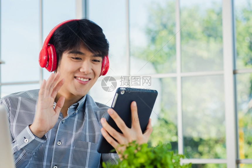 亚洲青年商人在使用数字平板电脑坐在办公桌式工作场所同时通过视频聊天会交谈和讨论打招呼时图片