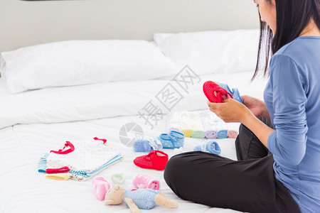 亚洲母亲准备婴儿衣物在床上休息和放松她为婴儿准备新生后购买的婴衣物图片