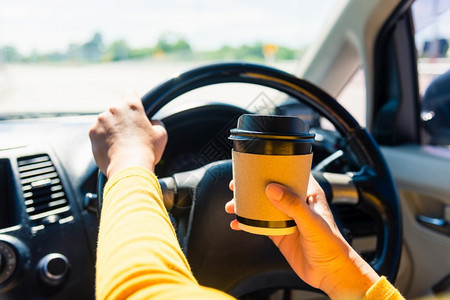 一位亚洲妇女早上在高速公路交通和车辆上上班时在车内和开车时喝热咖啡外卖杯图片