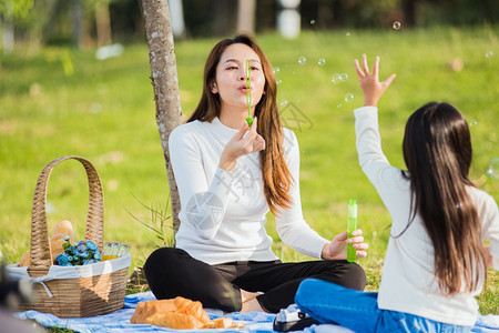 快乐的亚洲母亲和小女孩快乐的亚洲母亲和女儿玩得开心一起在户外享受快乐坐在草地上吹肥皂泡图片