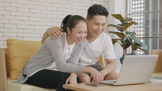 使用笔记本电脑网络摄像头技术在沙发上笑着的亚洲家庭幸福夫妇图片