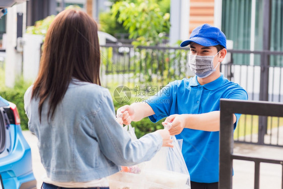 亚洲青年送货员戴面罩他制作杂货服务向在流行冠状动脉后在家中接受门的女顾客提供大米食品箱塑料袋回到新的正常概念图片