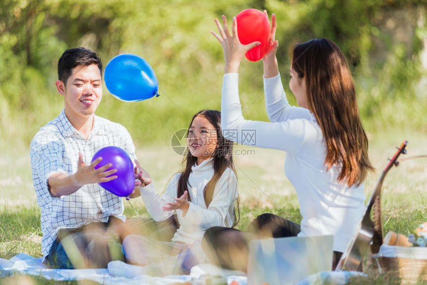 快乐的亚洲年轻家庭父亲母和小女孩在户外享受乐趣和坐在野餐毯子上夏季花园春公玩气球家庭放松概念图片